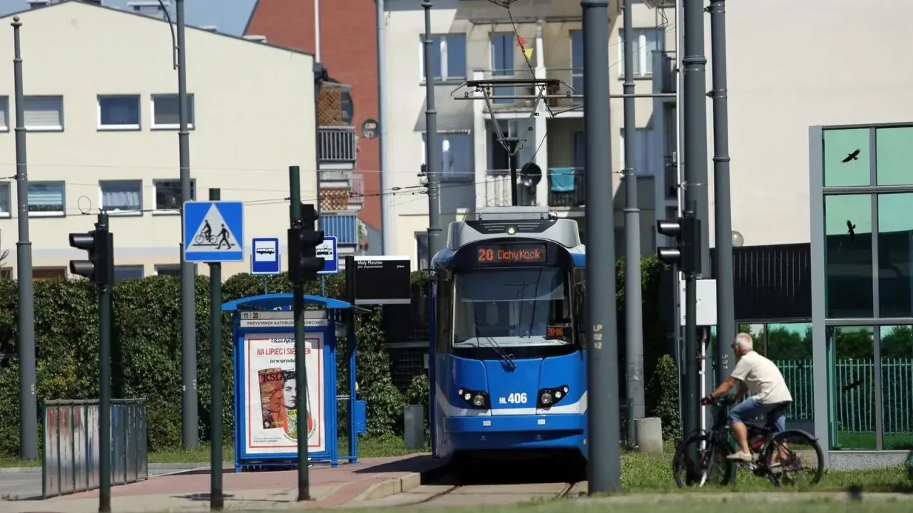 Niebieski tramwaj na przystanku w Krakowie, obok rowerzysta i znaki drogowe.