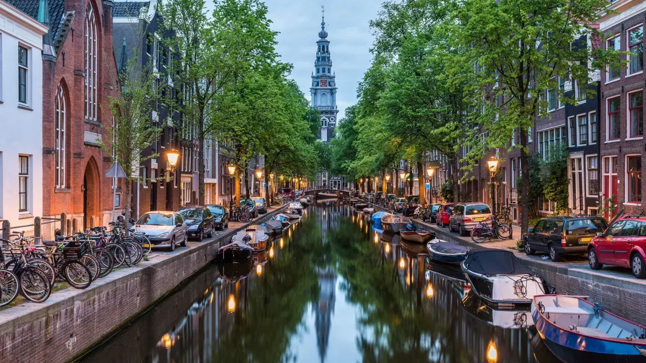 Kanał w Amsterdamie z łodziami, rowerami i wieżą kościelną w tle.