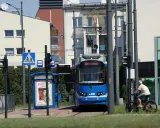 Niebieski tramwaj na przystanku w Krakowie, obok rowerzysta i znaki drogowe.