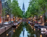 Kanał w Amsterdamie z łodziami, rowerami i wieżą kościelną w tle.
