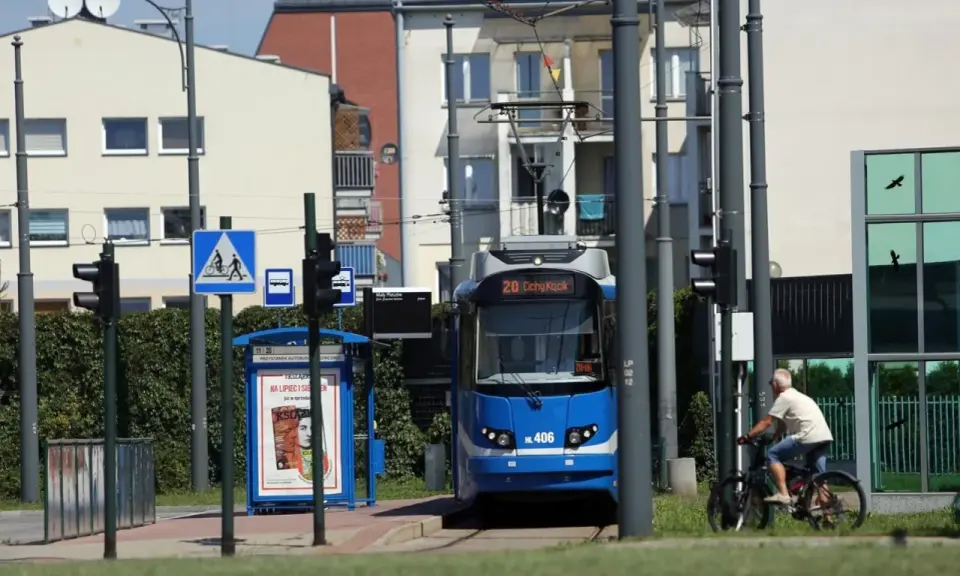 Niebieski tramwaj na przystanku w Krakowie, obok rowerzysta i znaki drogowe.